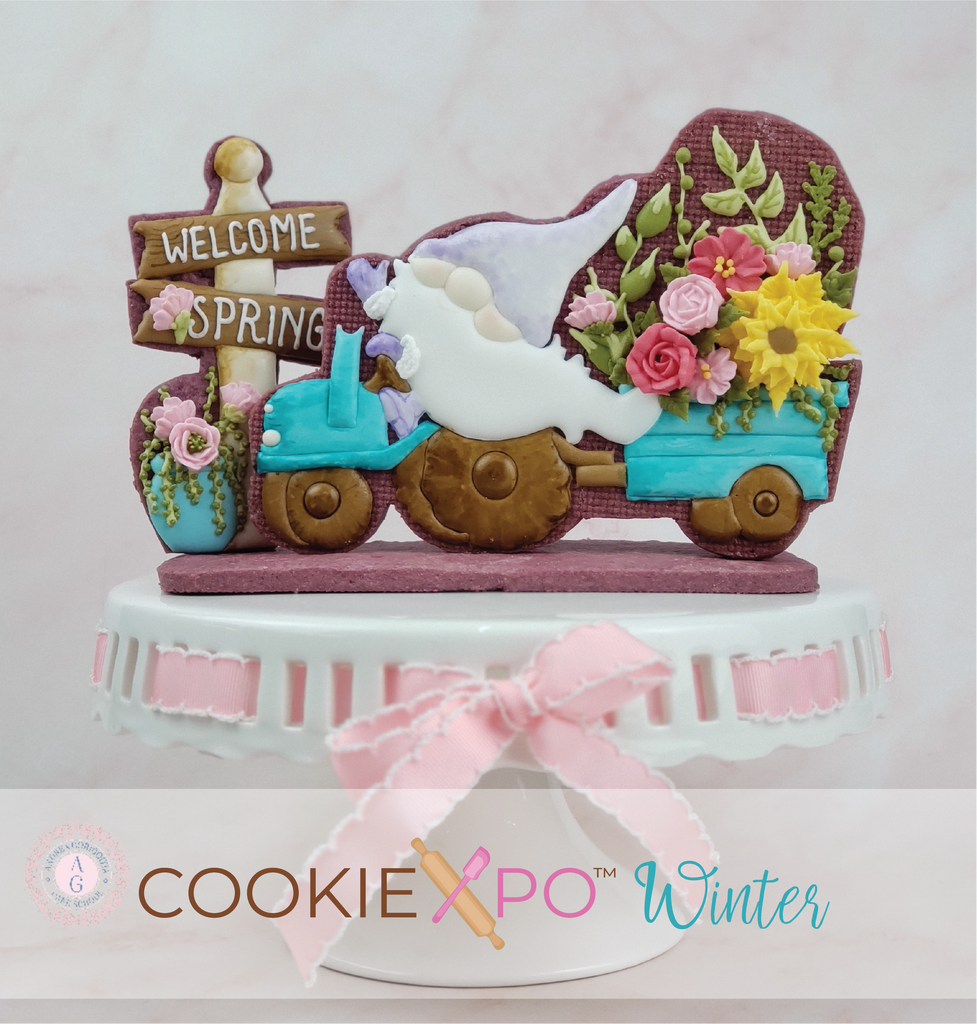 Sugartess custom cookie cutter for Cookiexpo 2021 in shape of a spring gnome driving a tractor pulling a cart filled with spring flowers. A sign reads "Welcome Spring" on the side.